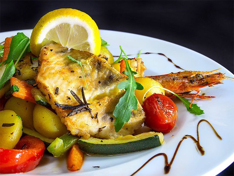 Gebratener Fisch mit Gemüse, Kartoffeln und Zitrone auf einem weißen Teller